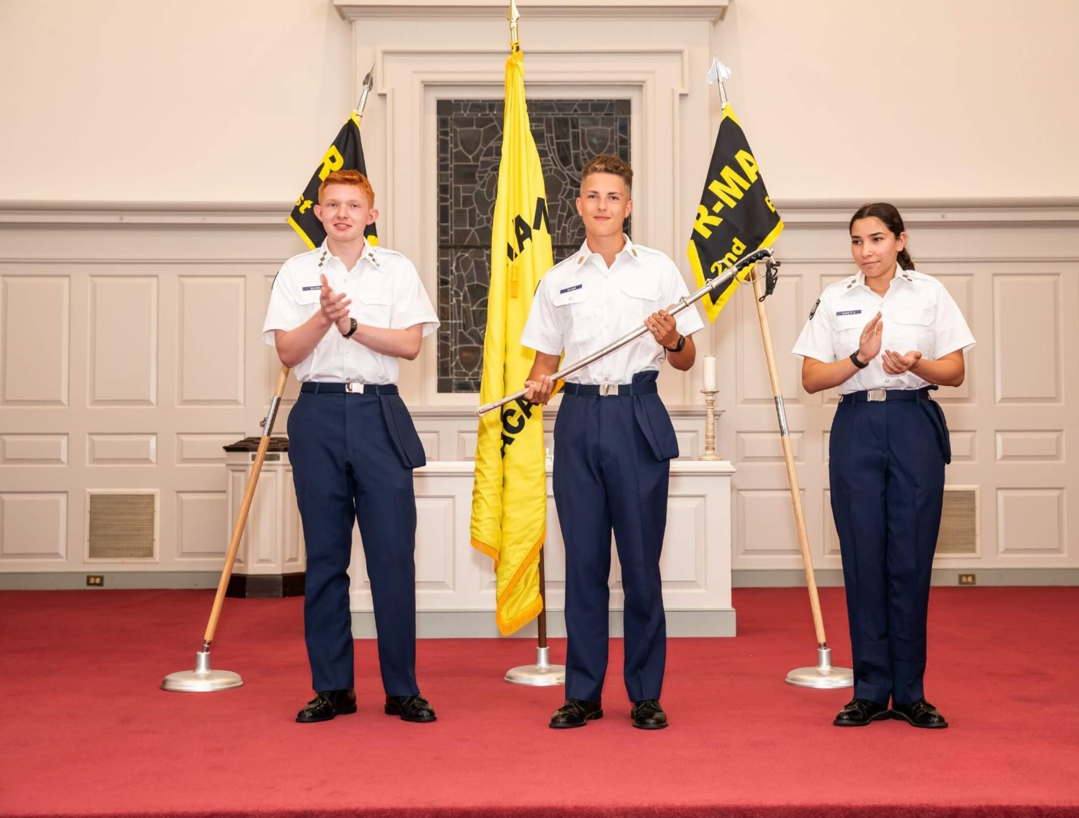 Three R-MA students in the Cadet Leadership Development Program on a stage clapping.