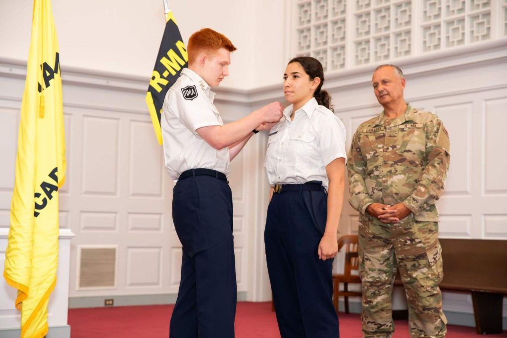 A private school student in uniform presenting their fellow student with an award on stage.