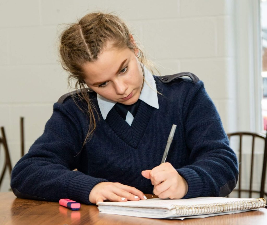 A focussed student at R-MA preparatory school writing at a desk