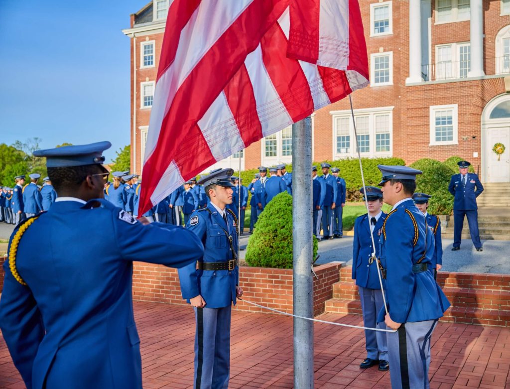 R-MA students in uniform raising the flag during a ceremony at a College Prep School.