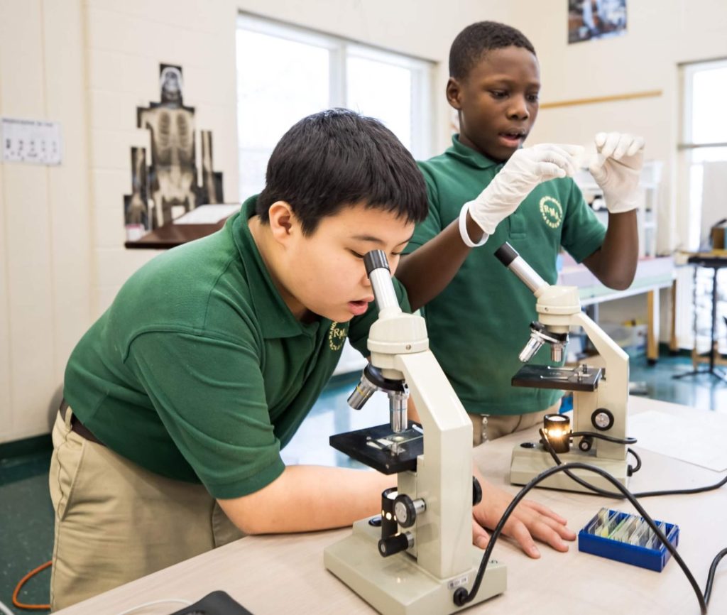 A pair of R-MA students doing a biology experiment with a microscope in a classroom