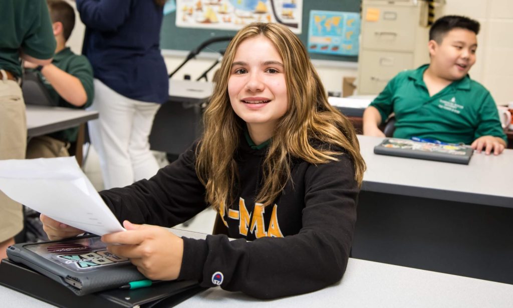 An R-MA student sitting at a desk holding a paper.