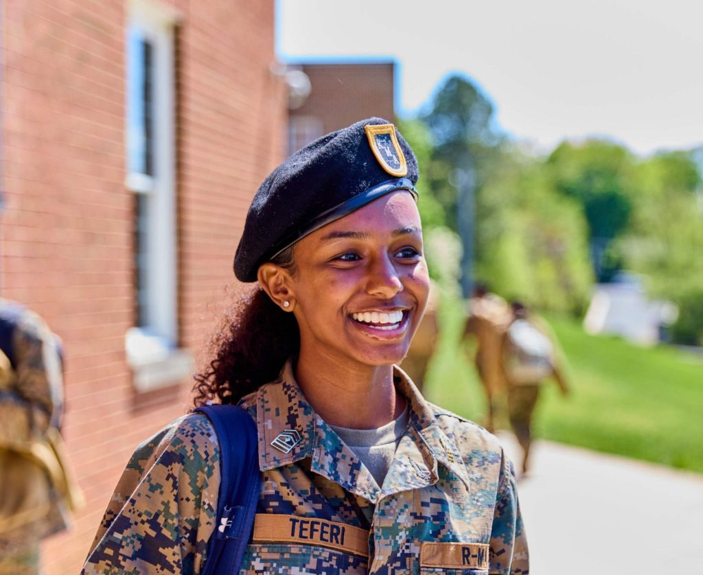 A smiling female student in military uniform walking outside at our college prep school, representing college readiness success