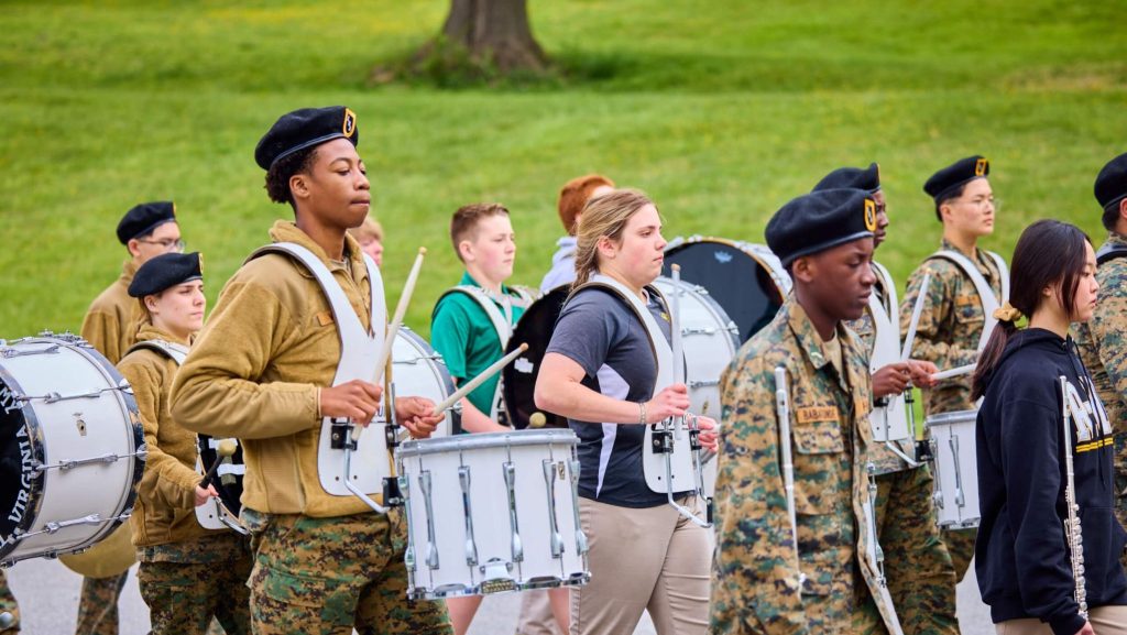 A group of students in band uniforms playing drums and marching at our college prep school, demonstrating teamwork and college readiness success