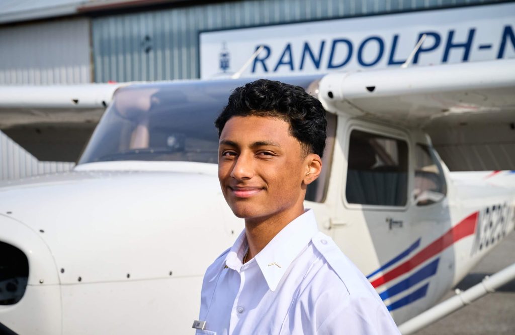 A smiling student standing beside a plane during flight training at private boarding school R-MA