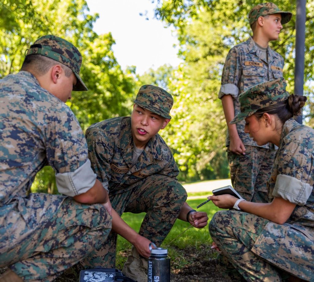 Cadets collaborating outdoors on a field exercise, demonstrating modern military concepts such as teamwork and decision-making
