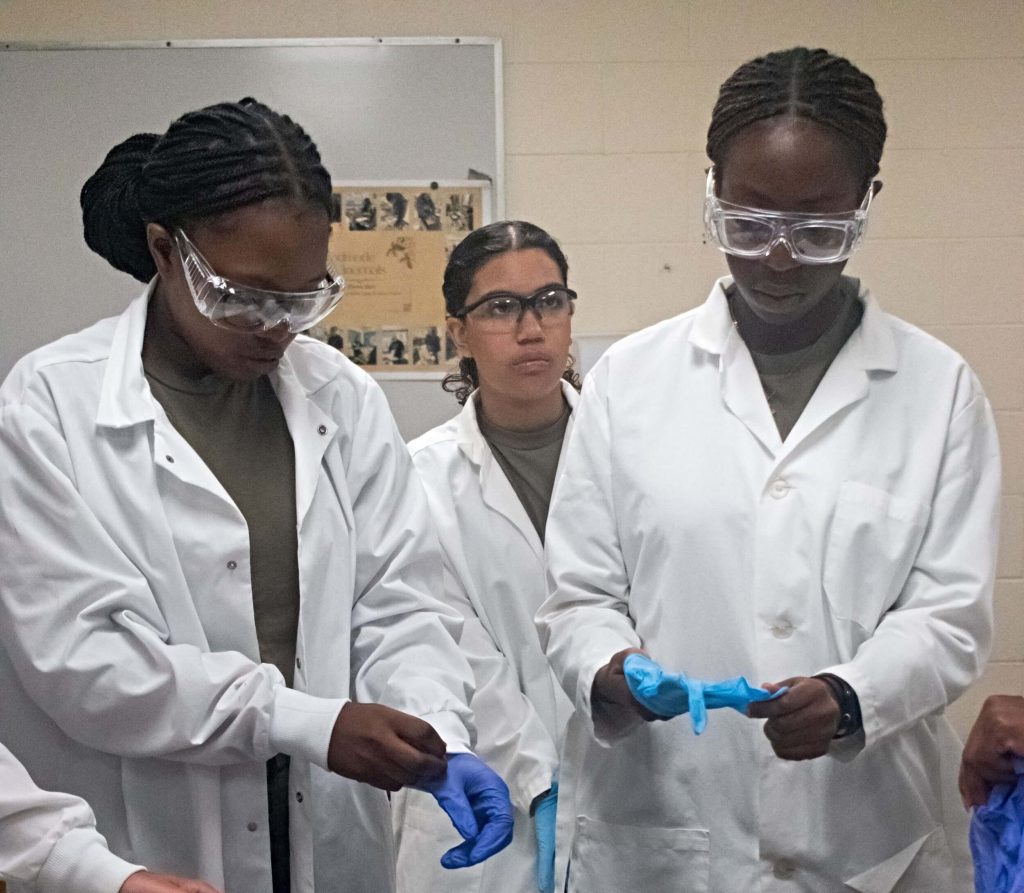 A pair of students wearing lab coats and safety goggles during a hands-on science lesson in a summer academic program