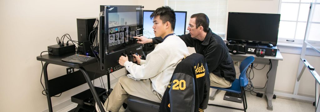 R-MA student using a flight simulator with guidance from a faculty instructor during a boarding school campus visit.