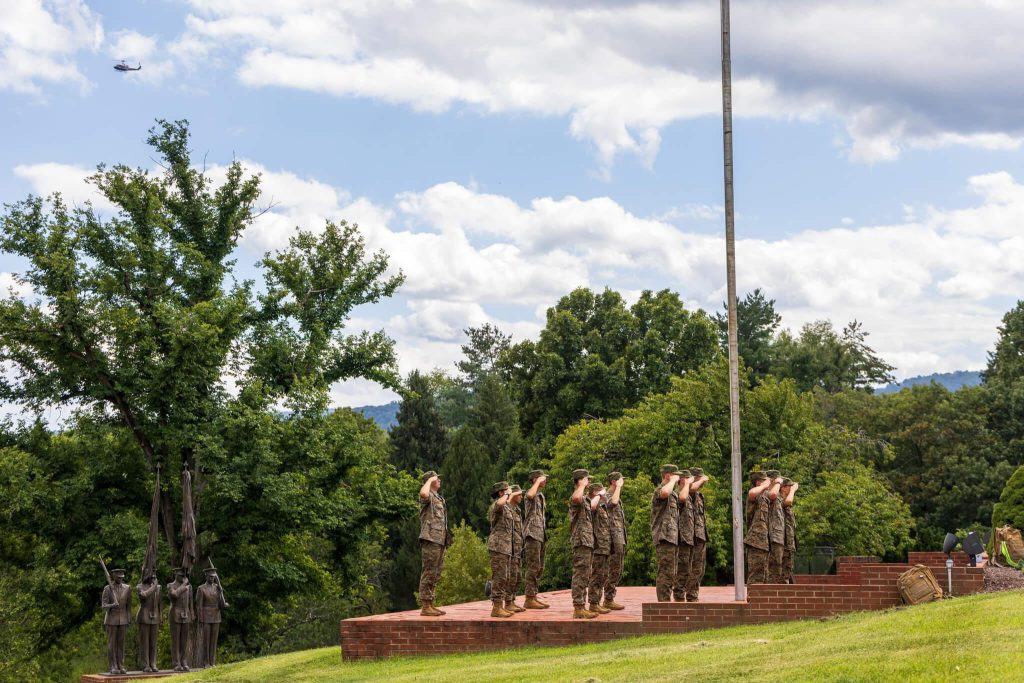 Randolph-Macon Academy cadets saluting during an outdoor formation as a helicopter passes overhead.